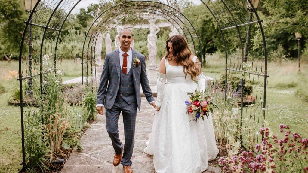 A newlywed couple walking hand in hand through the stunning gardens at Berwick Lodge, a romantic wedding venue in Bristol.