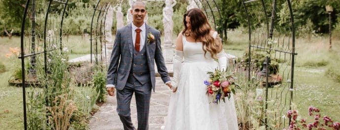A newlywed couple walking hand in hand through the stunning gardens at Berwick Lodge, a romantic wedding venue in Bristol.