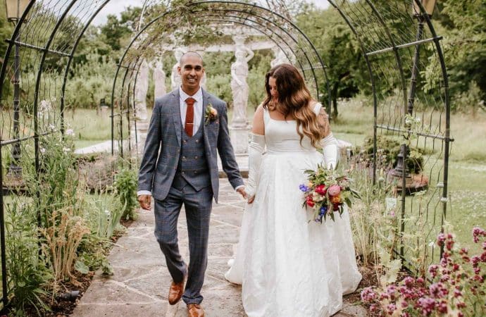 A newlywed couple walking hand in hand through the stunning gardens at Berwick Lodge, a romantic wedding venue in Bristol.